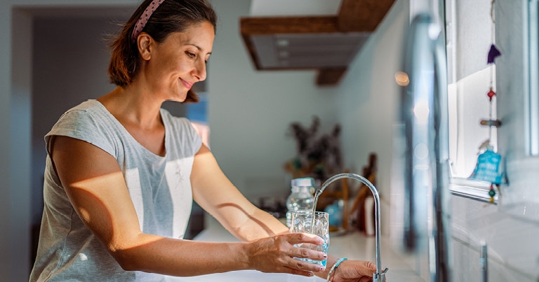 A woman fills a glass of water at a faucet with a water treatment system.