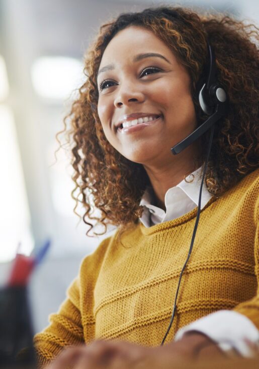 A young african american call center agent smiles and converses with a customer on a voice headset