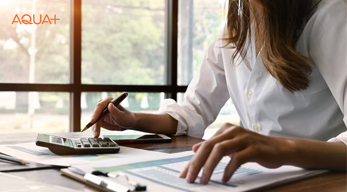 A woman sits at a desk with paperwork and a calculator.