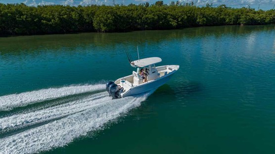 A boat buyer drives a boat along a waterway with trees lining the shore.